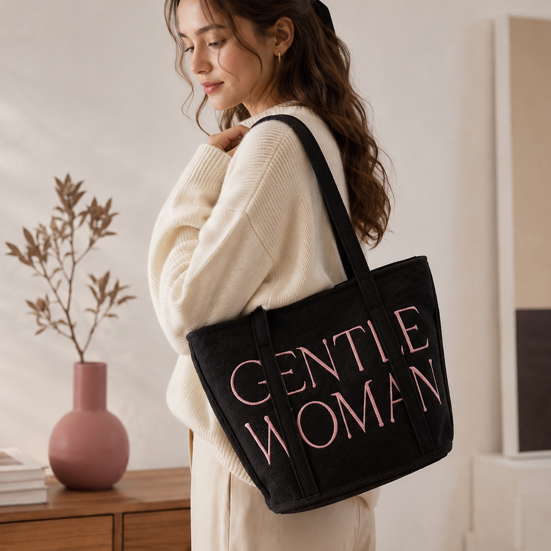 Woman holding a black tote bag with 'GENTLE WOMAN' text in a room setting.