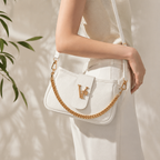 White handbag with gold chain strap held by a person against a neutral background