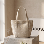 Beige tote bag with 'GENTLE WOMAN' text on a wooden surface.